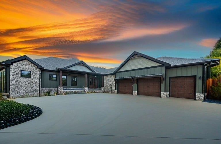 A modern home exterior featuring a mix of stone and siding with a three-car garage, framed against a vibrant sunset sky. The driveway and landscaping add to the curb appeal. | Paxisgroup