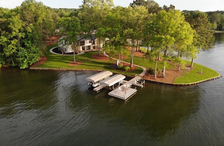 A picturesque lakeside property with a dock and boat slips, surrounded by vibrant green lawns, walking paths, and tall trees, viewed from the water. | Paxis Group